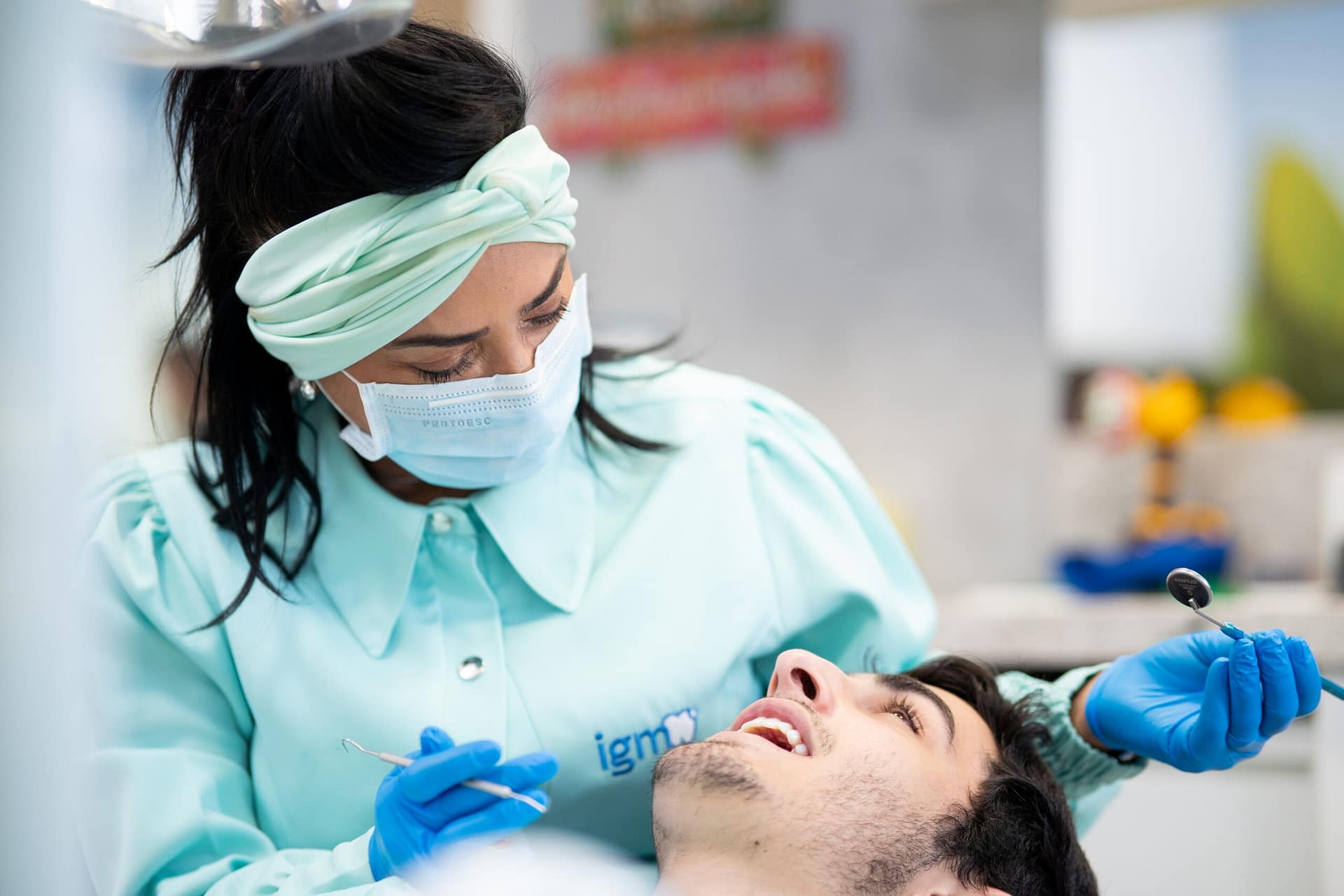 serviços odontológicos: dentista com jaleco azul claro atendendo um rapaz que está deitado na cadeira